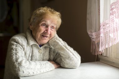 Yaşlı kadın masada oturuyor.