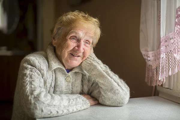 Starsza kobieta siedzi w pobliżu okna — Zdjęcie stockowe