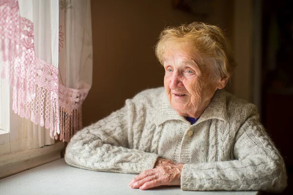 Oude vrouw zitten in de buurt van het venster — Stockfoto