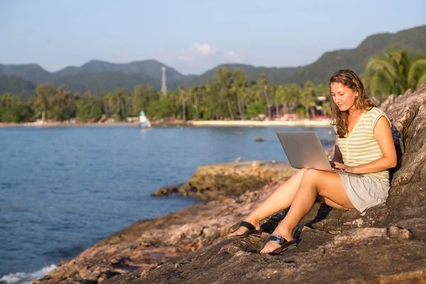 Kvinna sitter vid havets kust med laptop — Stockfoto