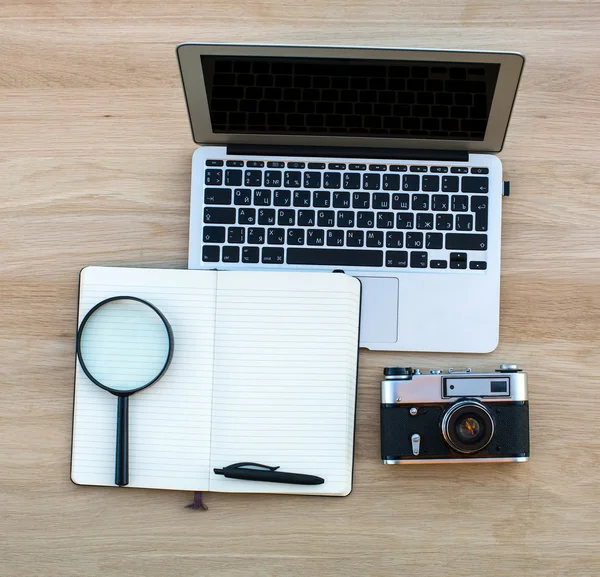 Laptop, Notepad magnifier and camera on table — Stock Photo, Image