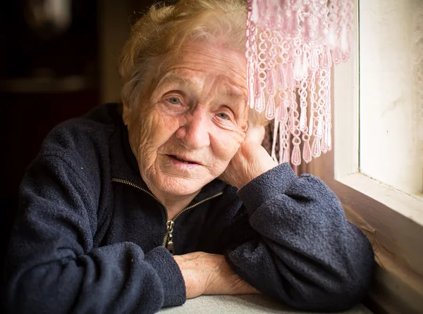 Old woman sitting near the window — Stock Photo, Image