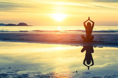 Kadın plajda yoga yapıyor.