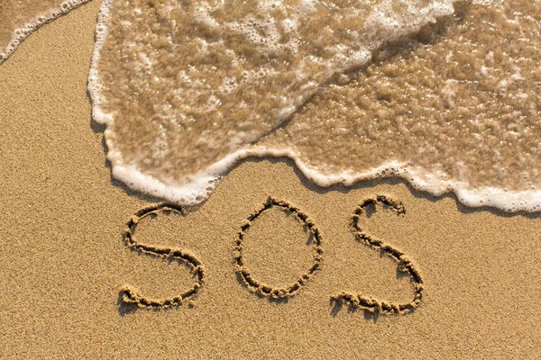 SOS - word dras på sandstrand — Stockfoto