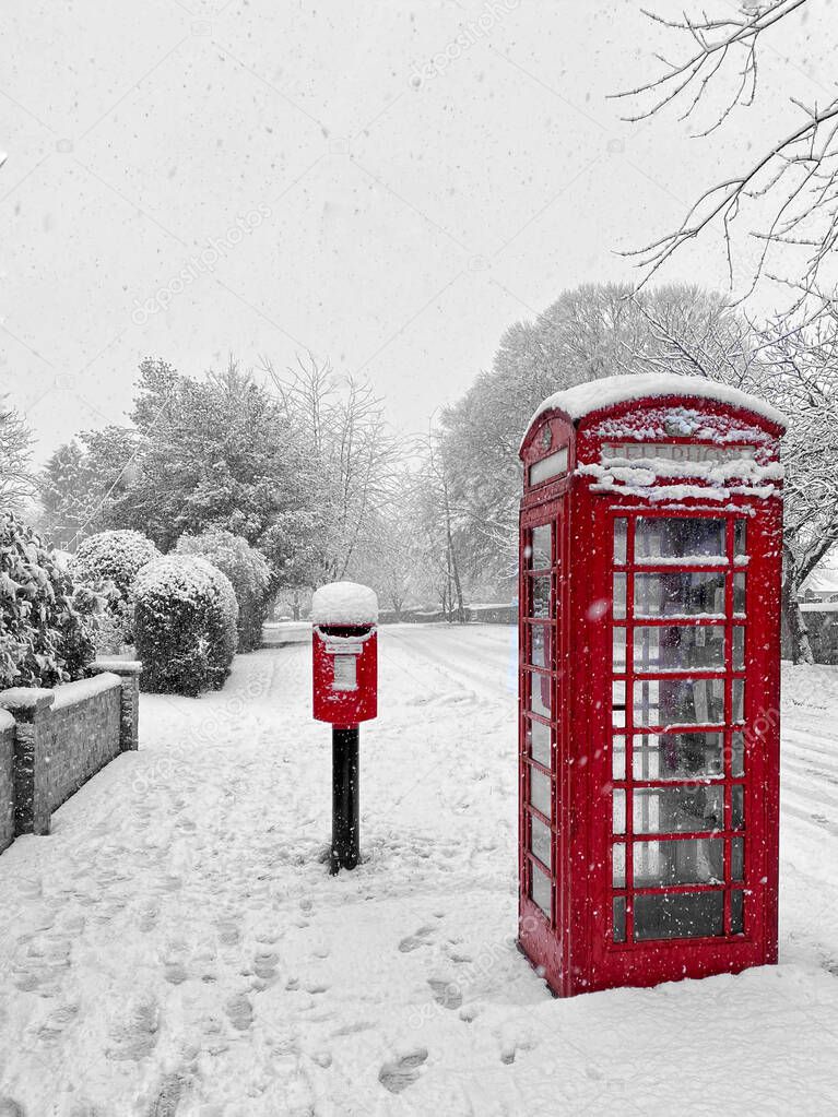 shot of a village post box and phone box in a snowstorm.  Red Post box and phone box on a black and white background