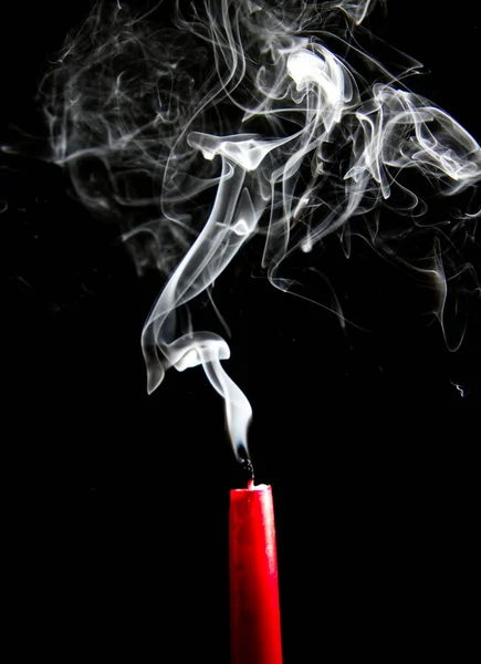 Smoke rising from an extinguished red candle against a black background