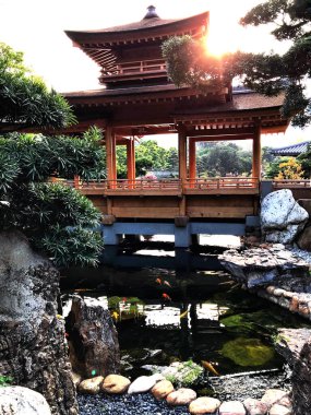 Hoonng Kong Parkı 'nda Pagoda tarzı bir köprü inşa edildi. Köprü içinde balık olan bir nehri kapsar. Güneş köprünün arkasından bakıyor. 