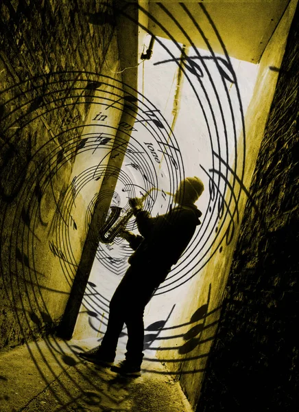 angled silhouette of a street saxophone player in a yellow light with music spilling from the sax