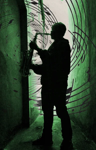 a street sax player silhouetted aganst a green light with music spilling from the sax