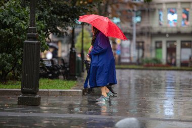 Lviv, Ukrayna - 30 Eylül 2020: Nike spor ayakkabısı ve kırmızı şemsiye giyen yaşlı kadın yağmurlu sokakta yürüyor