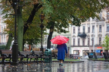 Lviv, Ukrayna - 30 Eylül 2020: Nike spor ayakkabısı ve kırmızı şemsiye giyen yaşlı kadın yağmurlu sokakta yürüyor