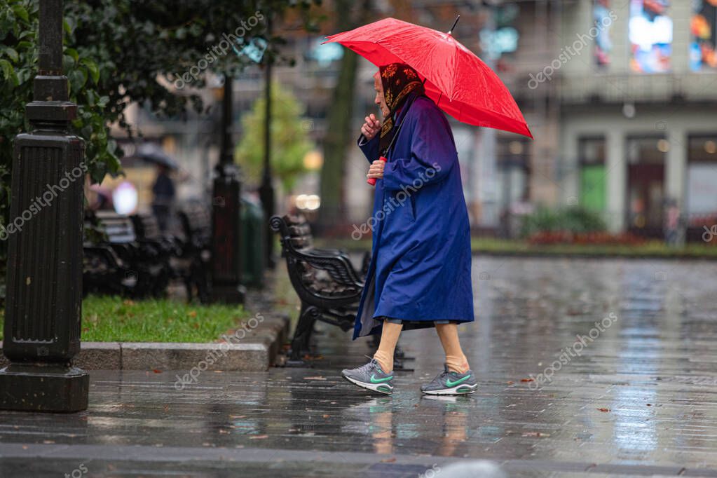 Lviv, Ukraine - September 30, 2020: senior woman wearing Nike sneakers and red umbrella walking on rainy street