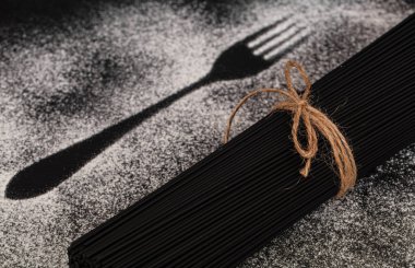 Arka planda bir deste siyah spagetti çatal ve un kaplı bıçak silueti var. Spagetti mürekkep balığı mürekkebi 