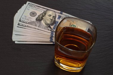 Bir bardak viski ve siyah arka planda 100 dolarlık banknotlar.