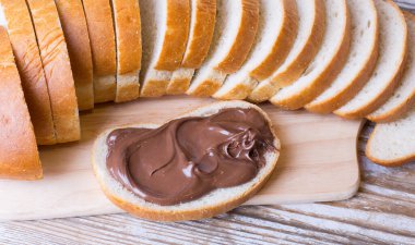 Bir somun ekmek ve ahşap zemin üzerinde çikolatalı fındık kremalı bir dilim ekmek. Çikolata ve fındık ezmeli lezzetli kahvaltı..