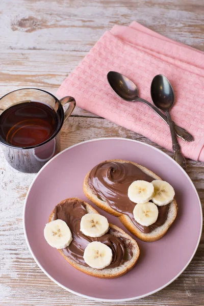 Chocolate-nut cream with banana on slices of bread with a Cup of tea. Delicious Breakfast with chocolate and nut paste with banana and a Cup of tea.