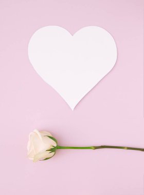 Soluk pastel pembe arka planda, altında beyaz gül olan basit bir kalp şekli kartı. Minimalist fikir.
