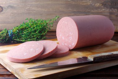 piece of whole raw pork bologna on cutting board with some slices. Italian food clipart