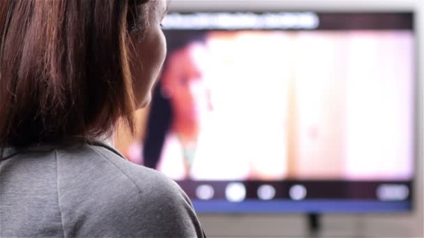 Молодая женщина с пультом дистанционного управления смотрит телевизор — стоковое видео