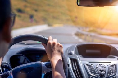 Girl hands on the steering wheel of a car while driving. Against the background, the windshield and road. Focus on her hand