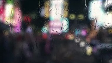Time Square 'de yağmur penceresinden New York manzarası. Geceleri şehrin bokeh ışıklarıyla yağmur damlaları yağıyor. Şehir trafiğinde yağmur yağıyor. 4k