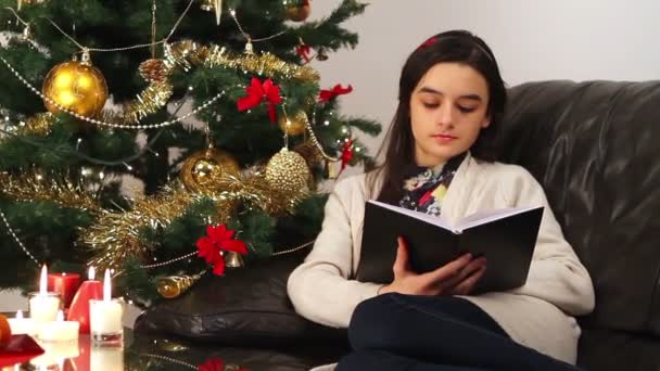 Girl reading a book while sitting near Christmas Tree — Stock Video