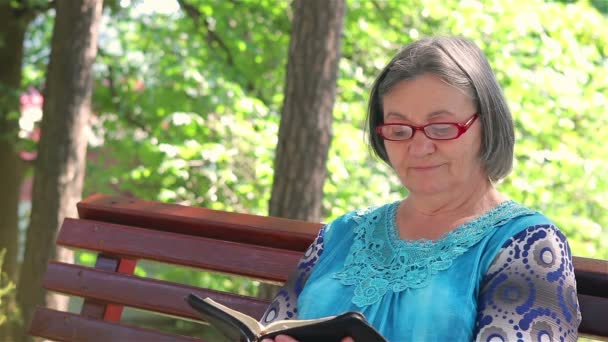 Пожилая женщина, читающая Библию на открытом воздухе — стоковое видео