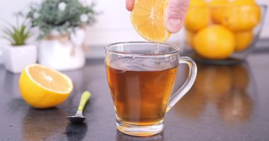 Mutfak tezgahında sıcak çayın içine sıkıştırılmış taze limon yakın plan. Sıcak çay ritüeli, doğal lezzet ve sağlıklı yaşam tarzı konsepti. Yavaş çekim