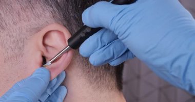 Tıbbi bir aletle erkek bir hastanın kulağından kulak kirini alan bir doktorun yakın çekimi. ENT bakımı, hijyen ve profesyonel sağlık prosedürü kavramı.