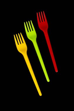 Siyah zemin üzerinde üç plastik tek kullanımlık çatal bıçak çatalı sarı, yeşil ve kırmızı (Litvanya bayrağı renkleri) izole
