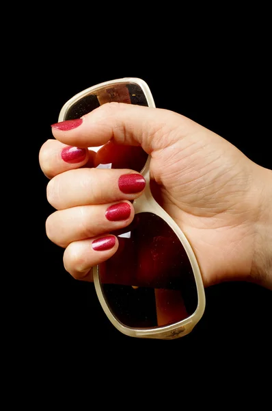 Mão feminina segurando óculos de sol no fundo preto — Fotografia de Stock