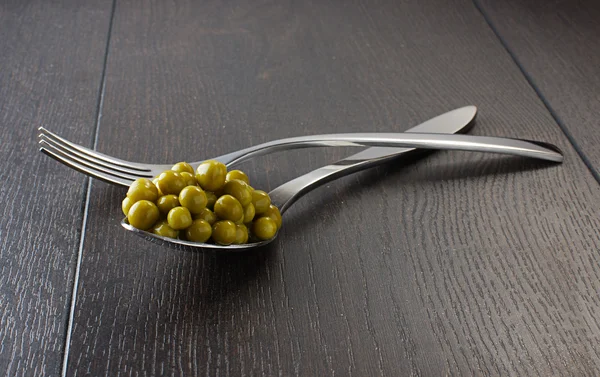 Piselli nel cucchiaio e forchetta sul tavolo di legno scuro — Foto Stock