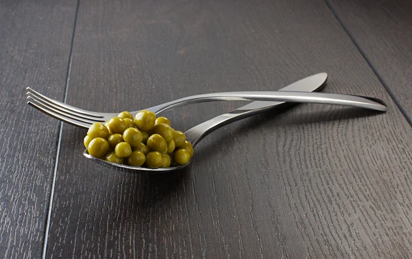 Peas in the spoon and fork on the dark wooden table — Stock Photo, Image