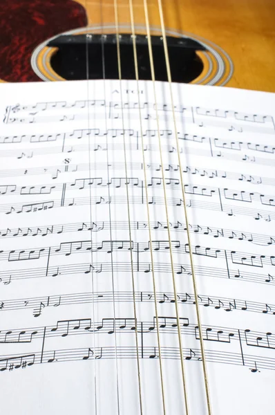 Sheet music notes under six guitar strings — Stock Photo, Image