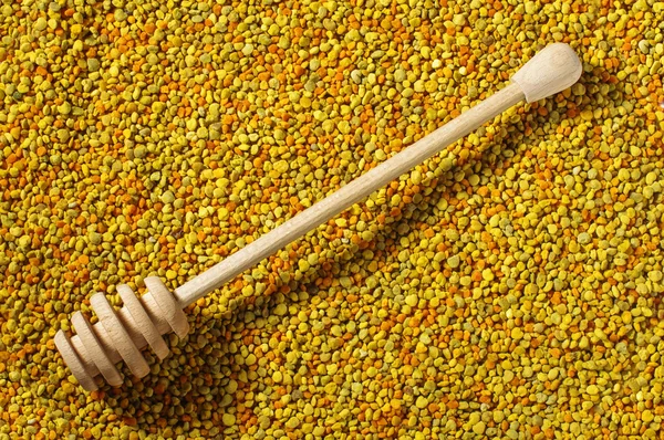 Wooden honey dipper on bee pollen granules surface — Stock Photo, Image