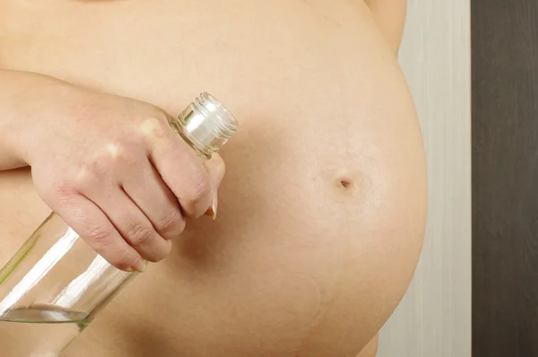 Pregnant belly and woman holding vodka bottle — Stock Photo, Image