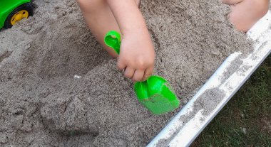 Küçük çocuk dışarıda oyun alanında kum havuzunda oynuyor. Renkli kum oyuncakları olan çocuk. Dışarıda sağlıklı, aktif bir bebek.