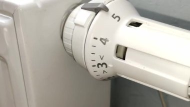 Erkek eli radyatörün üzerindeki termostatın beyaz sapını büker.