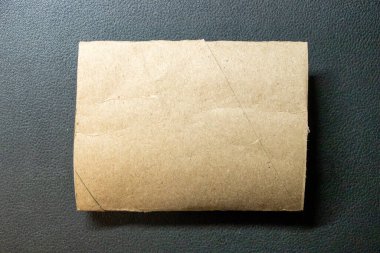 Kahverengi dikdörtgen kağıttan bir çarşaf koyu bir yüzeyde duruyor. Eğitimsel amaçlar veya sürdürülebilirlik ve geri dönüşüm kavramları için kullanışlı.