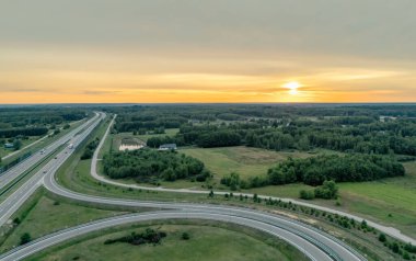 Bereketli bir gün batımı altında yemyeşil bir otobanın hava manzarası. Sahne, altyapıyla harmanlanmış doğanın sükunetini yakalıyor..