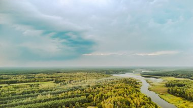 Bulutlu bir gökyüzünün altındaki yemyeşil ormanlarda süzülen sakin bir nehrin havadan görünüşü doğanın güzelliğini ve huzurunu yakalıyor..