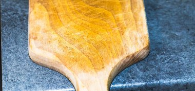 Gri bir tezgahta dinlenen tahta bir pizza küreği pürüzsüz yüzeyi ve doğal tahılını sergiliyor. Mutfak ve restoranlarda pişirme ve aşçılık sunumları için ideal..