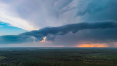 Uçsuz bucaksız yeşil orman manzarasının üzerindeki dramatik gökyüzünün hava görüntüsü ufku aydınlatan güneş ışığıyla dinamik bulutlar sergiliyor. Doğanın gücü ve güzelliği sergileniyor.