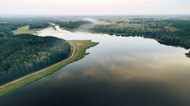 Bereketli yeşillikler ve ormanlarda süzülen sakin bir nehrin havadan görünüşü su yüzeyindeki bulutların yansımasını gösteriyor..
