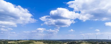 Parlak mavi gökyüzünün altındaki yeşil tepelerdeki bir rüzgar çiftliğinin panoramik görüntüsü. Rüzgar türbinleri görülebilir yenilenebilir enerji ve doğada sürdürülebilir bir gelecek sergiliyorlar..