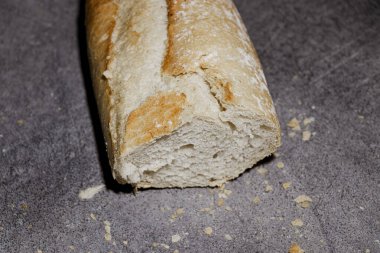 Taze pişmiş bir baget. Yumuşak, havadar iç yüzünü gösteriyor. Sahne, ekmek kırıntılarının etrafa saçıldığı bir kırsal mutfak tezgahı..