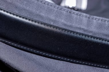 Dikiş detaylarını vurgulayan desenli kumaş arka planına karşı parlak siyah deri bir kayış yakın plan. Moda ve tasarım bağlamları için mükemmel.