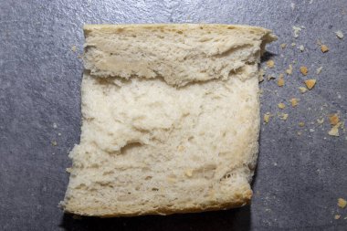 Yumuşak kabarık dokusu olan bir parça ekmeğin yakın çekimi. Koyu bir taş zemin üzerinde kırıntıları gösteriyor. Tazelik ve rahatlığı gösteren yemek fotoğrafçılığına uygun..