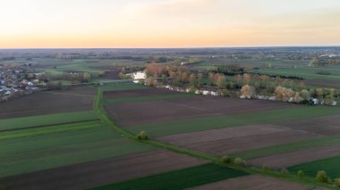 Gün batımında yemyeşil tarlaların ve dolambaçlı bir nehrin havadan görünüşü. Canlı bir gökyüzünün altında tarım arazileri ve uzak ormanlar olan kırsal manzara..