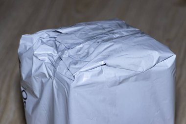Ahşap bir yüzey üzerinde dinlenen buruşuk gri bir paketin yakın plan görüntüsü nakliye ve ambalaj üzerine tartışmalar için uygun buruşuk materyalin kusurlarını ve dokularını vurguluyor.